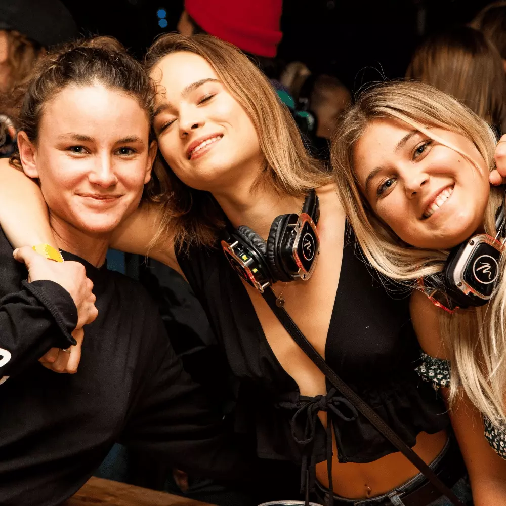 Three friends smiling together at camera with silent disco headsets around their necks